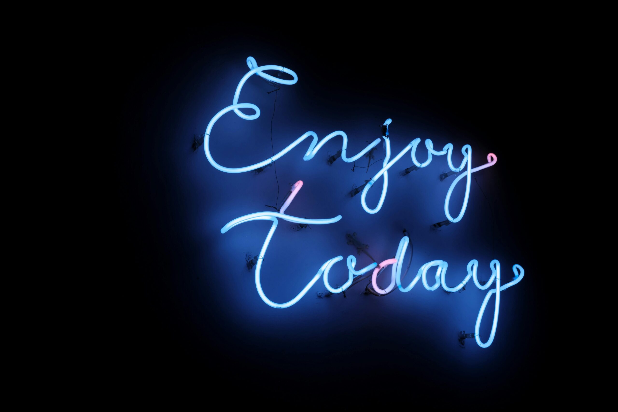 Bright blue neon sign with the phrase 'Enjoy Today' on a dark background, creating a vibrant and uplifting atmosphere.